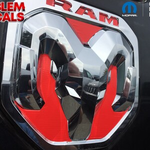 May include: Chrome and red RAM emblem decal. The emblem features a shiny chrome finish with red accents. The word "RAM" is visible in red at the top. The decal is an official licensed product.