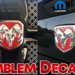 May include: Two red and chrome Ram emblem decals. The decals are on a black truck grille. The text "OFFICIAL LICENSED PRODUCT" and the Mopar logo are visible in the background. The text "EMBLEM DECALS" is in red at the bottom of the image.