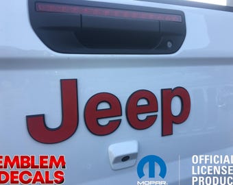 May include: Red Jeep emblem decal with black outline. The decal is attached to a white vehicle. The text "EMBLEM DECALS" is visible in the lower left corner. The text "OFFICIAL LICENSED PRODUCT" is visible in the lower right corner. The text "MOPAR" is visible below the Mopar logo.