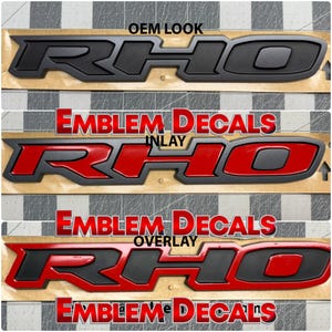 May include: Three different styles of "RHO" car emblems. The top emblem is black with a grey outline. The middle emblem is red with a grey outline. The bottom emblem is red with a grey outline. The text "EMBLEM DECALS" appears above each emblem.