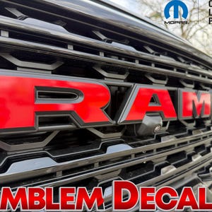 May include: Close-up of a black vehicle grille with the red "RAM" emblem. The words "Emblem Decals" are at the bottom. The official Mopar licensed product logo is in the top right corner.