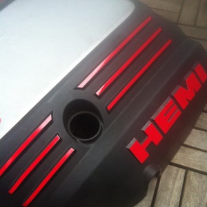 May include: Black engine cover with red "HEMI" lettering and red stripes. The cover has a round opening and a Mopar logo. "OFFICIAL LICENSED PRODUCT" is printed on the cover.  "EMBLEM DECALS" is printed below the cover.