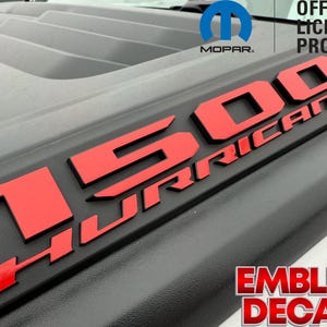 May include: Black vehicle emblem with the text "1500 HURRICANE" in red. The emblem is an official licensed product from MOPAR. The words "EMBLEM DECALS" are also visible in red.