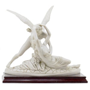 Puede incluir: Una escultura de mármol blanco que representa el mito griego de Cupido y Psique. La escultura muestra a Cupido con alas, abrazando a Psique. La escultura se exhibe sobre una base de madera oscura.