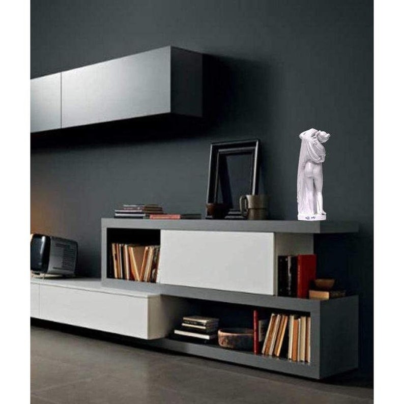 Puede incluir: Escultura blanca de dos figuras abraz&aacute;ndose, expuesta en una estanter&iacute;a con libros y un cuadro enmarcado. La estanter&iacute;a est&aacute; hecha de madera y tiene un acabado blanco y gris.