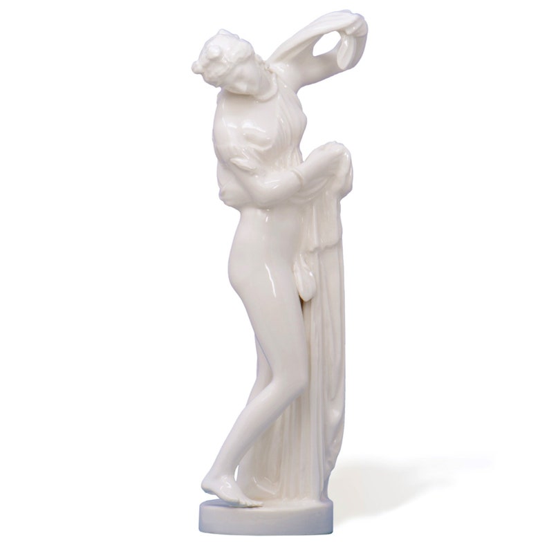 Puede incluir: Una figurita de porcelana blanca de una mujer de pie con los brazos en alto, sosteniendo una cortina. La figurita es de estilo cl&aacute;sico y es una pieza decorativa.