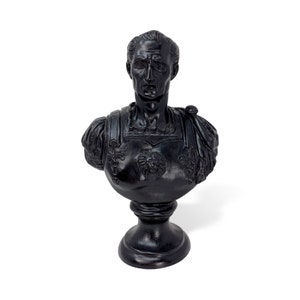 May include: Black and white bust sculpture of a man wearing a toga with a lion on his chest. The bust is on a black pedestal.