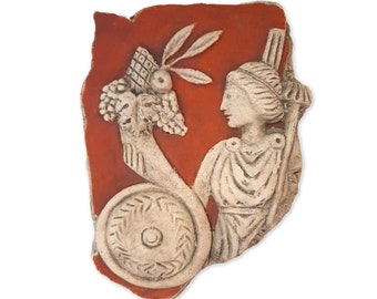 May include: A carved relief sculpture featuring a classical figure holding a shield and a cornucopia of fruits and foliage. The sculpture is off-white with a red background. The artwork is reminiscent of ancient Greek or Roman art.