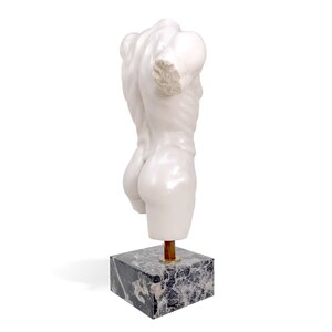 May include: White marble sculpture of a torso on a black and white marble base.