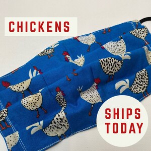 May include: A blue fabric face mask with a white and black chicken pattern. The mask has pleats and is sewn with white thread. The text "CHICKENS" is printed in red at the top of the image. The text "SHIPS TODAY" is printed in red at the bottom of the image.