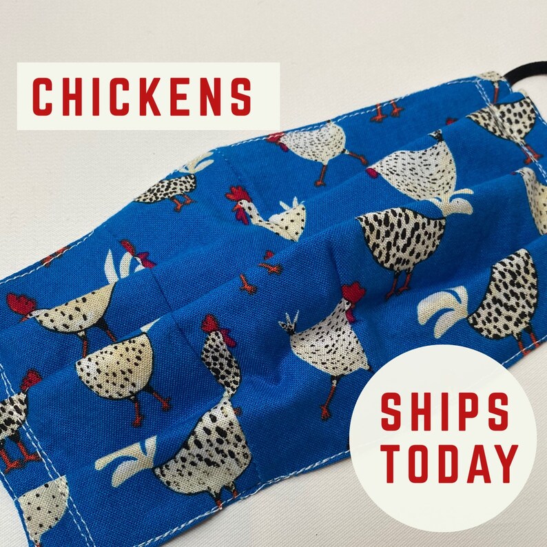 May include: A blue fabric face mask with a white and black chicken pattern. The mask has pleats and is sewn with white thread. The text "CHICKENS" is printed in red at the top of the image. The text "SHIPS TODAY" is printed in red at the bottom of the image.