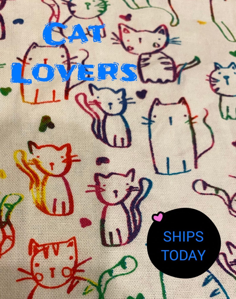 May include: White fabric with a colorful, hand-drawn pattern of cats. The text "CAT LOVERS" is written in blue letters across the top of the fabric. A black circle with the text "SHIPS TODAY" is in the lower right corner.
