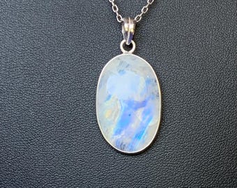 May include: A silver-toned necklace featuring an oval-shaped moonstone pendant with iridescent blue and white flashes. The pendant is suspended from a delicate, thin metal chain, showcasing a smooth, polished surface and a simple, clean setting.