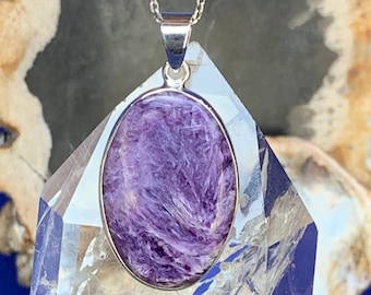May include: A silver chain necklace with a purple and silver oval pendant. The pendant features a natural stone with a swirling pattern.