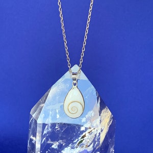 Op de afbeelding: Een zilveren ketting met een witte schelp hanger. De hanger heeft de vorm van een traan en heeft een spiraalvormig patroon.