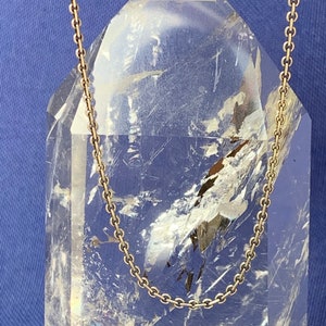 May include: A gold chain necklace on a clear crystal point. The chain is a simple, delicate design.