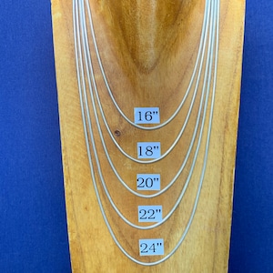 May include: Five silver snake chains of different lengths displayed on a wooden mannequin. The chains are labelled 16", 18", 20", 22", and 24".