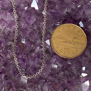 May include: A silver chain necklace on a bed of purple amethyst crystals. A Canadian dollar coin is next to the necklace for size reference.