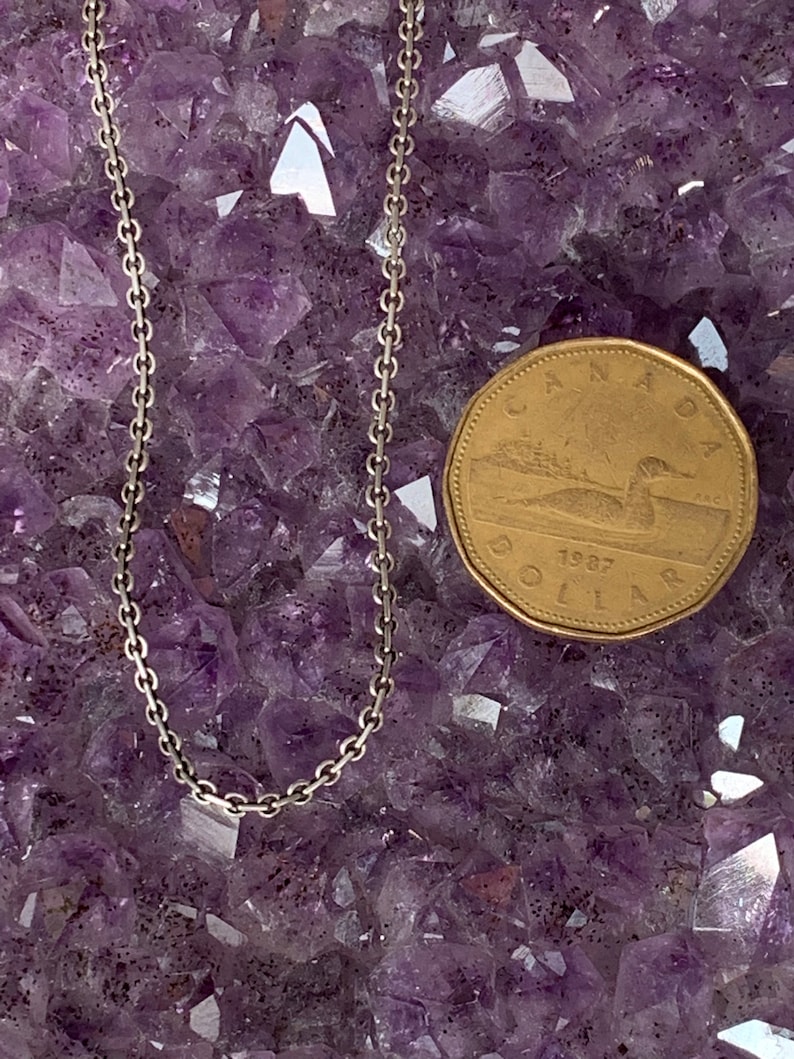 May include: A silver chain necklace on a bed of purple amethyst crystals. A Canadian dollar coin is next to the necklace for size reference.