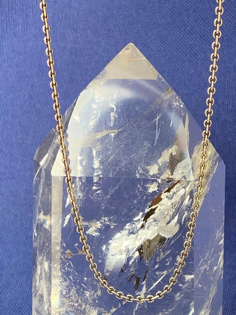 May include: A gold chain necklace on a clear crystal point. The chain is a simple, delicate design.