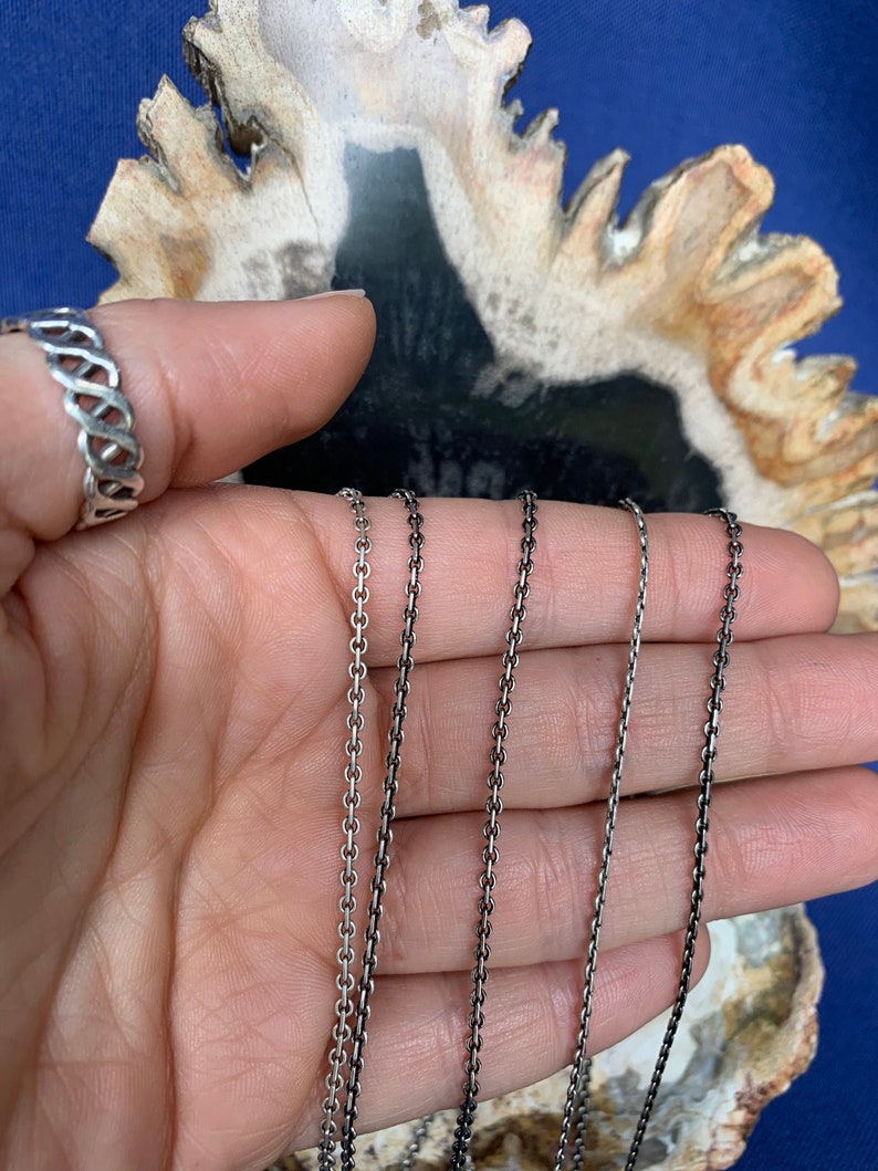 May include: Four silver chains of varying lengths, displayed on a hand against a background of a polished agate stone.