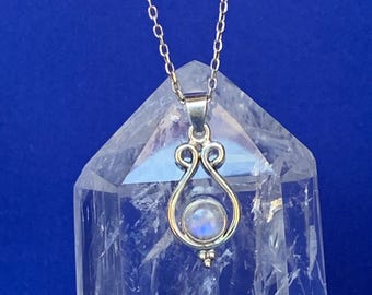 May include: A silver-toned pendant necklace featuring a teardrop-shaped design with a small, round, iridescent stone. The pendant hangs from a delicate chain. The necklace is displayed against a blue background.