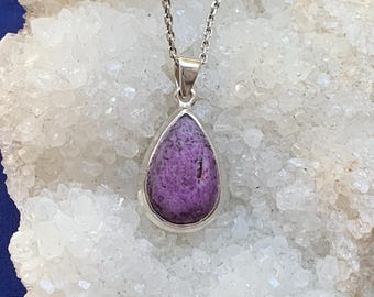 May include: A teardrop-shaped purple stone pendant set in a polished silver bezel, suspended from a delicate silver chain. The stone features a textured, mottled surface with deep violet and lighter lavender tones throughout the piece.