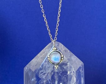May include: A silver-toned necklace featuring a circular pendant with a central iridescent cabochon stone. The pendant is suspended from a delicate link chain, showcasing a polished metal frame with small decorative bead accents at the top and bottom.