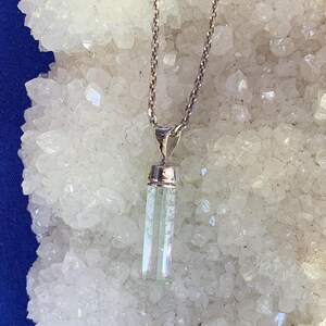 May include: A silver-toned metal chain necklace featuring a vertical, rectangular, pale green translucent crystal pendant capped with a polished silver-toned metal bail. The pendant hangs straight down from the center of the delicate link chain.
