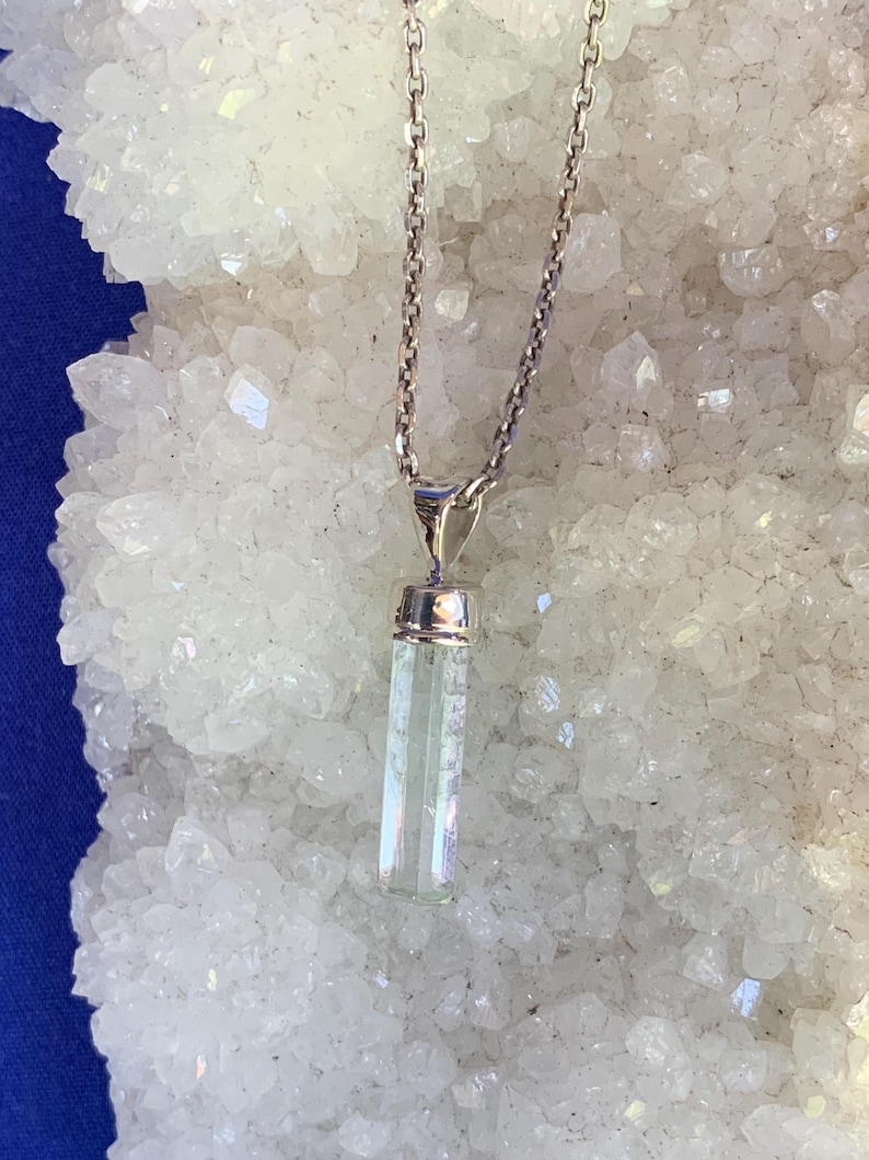 May include: A silver-toned metal chain necklace featuring a vertical, rectangular, pale green translucent crystal pendant capped with a polished silver-toned metal bail. The pendant hangs straight down from the center of the delicate link chain.