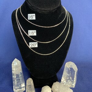 May include: Three silver chains of different lengths, 16 inches, 18 inches, and 20 inches, displayed on a black velvet mannequin. The chains are on a blue background with clear quartz crystals.