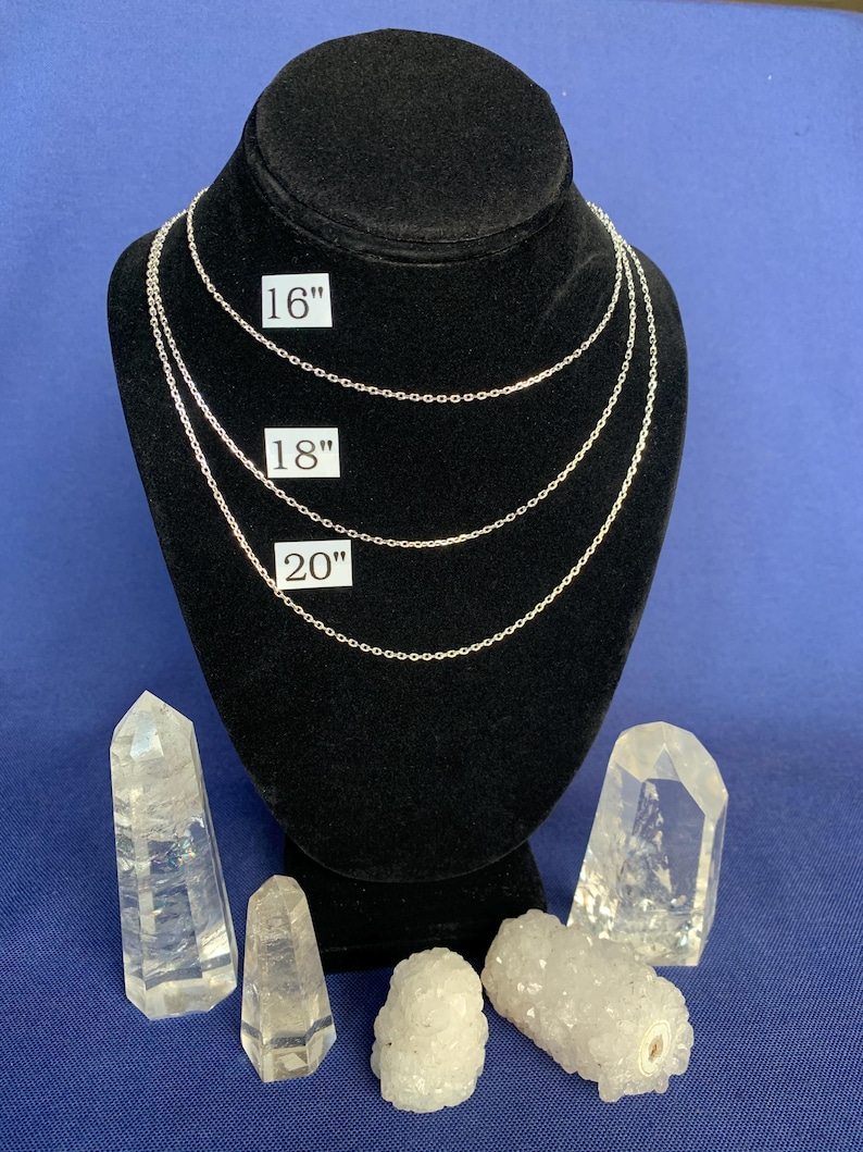 May include: Three silver chains of different lengths, 16 inches, 18 inches, and 20 inches, displayed on a black velvet mannequin. The chains are on a blue background with clear quartz crystals.