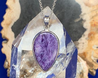 May include: A silver chain necklace with a purple and white teardrop-shaped pendant. The pendant is set in a silver bezel and has a swirling pattern.