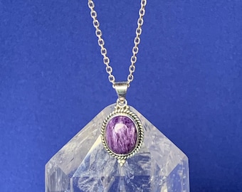 Peut inclure: Un collier à chaîne en argent avec un pendentif ovale en charoïte violette entouré d'une bordure en corde torsadée. Le pendentif est suspendu à une fine chaîne à maillons en argent, révélant les motifs tourbillonnants violets et blancs.