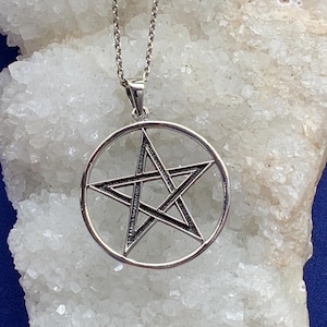 Op de afbeelding: Een zilveren ketting met een hanger met een pentagram, of vijfpuntige ster, in een cirkel. De hanger is aan een zilveren ketting.