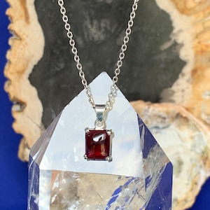 May include: A silver chain necklace with a square red gemstone pendant.
