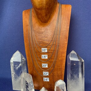 May include: Five silver chain necklaces of varying lengths displayed on a wooden mannequin. The necklaces are labeled with their lengths in inches: 16", 18", 20", 22", and 24".  The mannequin is surrounded by six clear quartz crystal points.