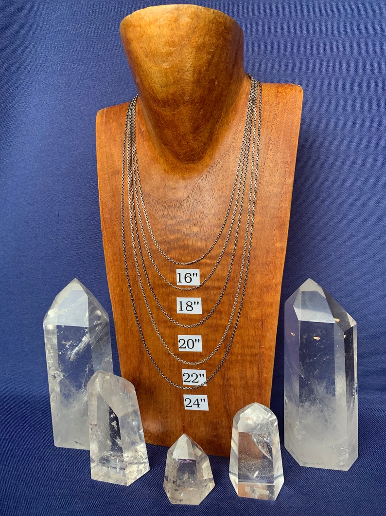 May include: Five silver chain necklaces of varying lengths displayed on a wooden mannequin. The necklaces are labeled with their lengths in inches: 16", 18", 20", 22", and 24".  The mannequin is surrounded by six clear quartz crystal points.