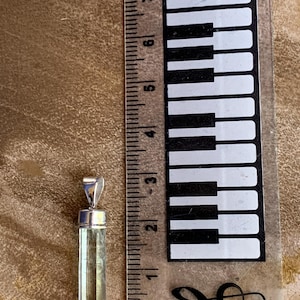 May include: A pale green, rectangular, faceted gemstone pendant with a silver-toned metal bail. The pendant is positioned next to a ruler, showing a length of approximately 1.25 inches from the top of the bail to the bottom of the stone.