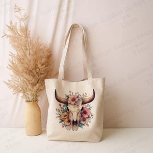 May include: A white canvas tote bag with a floral skull design. The skull is surrounded by pink, yellow, and green flowers. The bag has two handles.