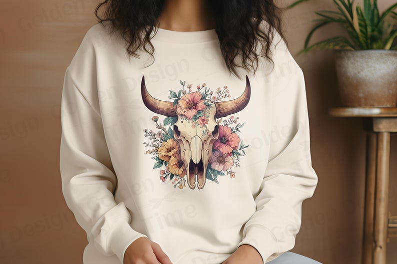 May include: A white sweatshirt with a floral design featuring a bull skull. The skull is surrounded by pink, yellow, and orange flowers.