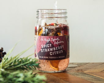 May include: A glass jar filled with fruit and spices, being poured into with a clear liquid. The jar has a label that reads "The High Spirits Infusions Spicy Strawberry Citrus Best with Rum, Tequila or Mezcal."