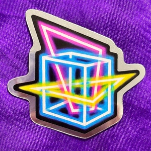 May include: A silver sticker with a neon blue, pink, and yellow geometric design. The design features a cube with lines intersecting through it.