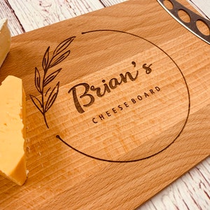 May include: A wooden cheese board with a circle design engraved with the text "Brian's Cheese Board". The board has two pieces of cheese on it.