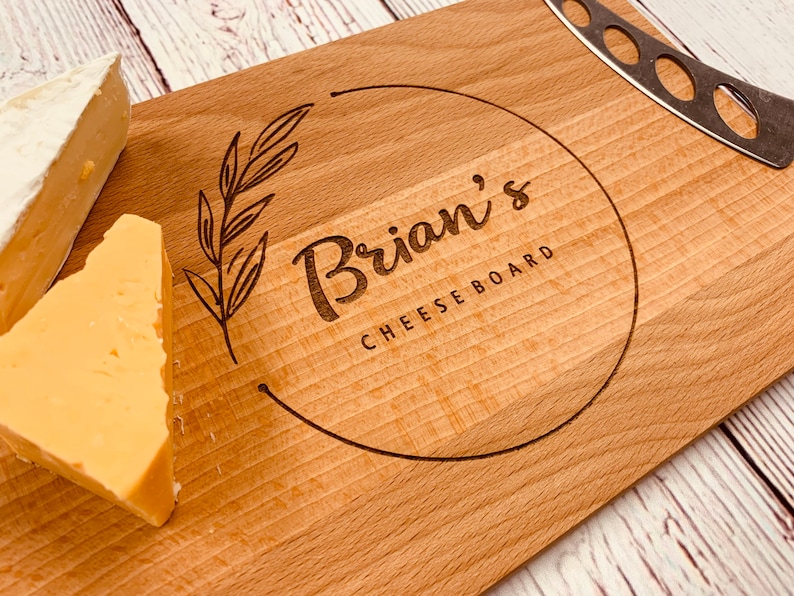 May include: A wooden cheese board with a circle design engraved with the text "Brian's Cheese Board". The board has two pieces of cheese on it.