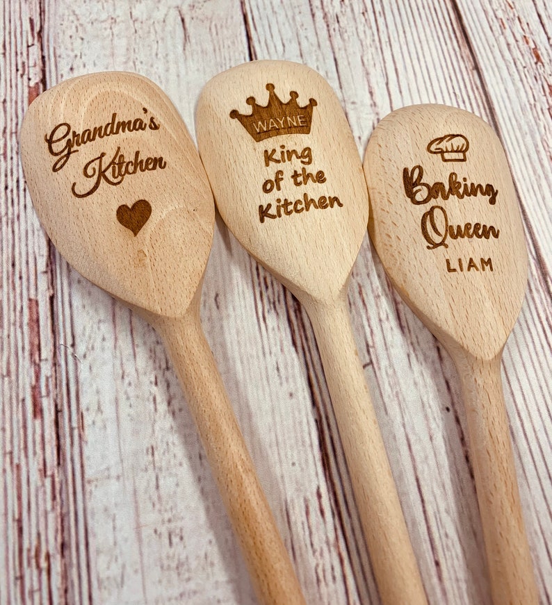 May include: Three wooden spoons with engraved text. The first spoon says "Grandma's Kitchen" with a heart. The second spoon says "Wayne King of the Kitchen" with a crown. The third spoon says "Liam Baking Queen" with a chef's hat.