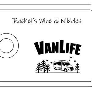 May include: A rectangular serving board with a rounded cutout on the left side. The board features the text Rachel's Wine & Nibbles at the top and a graphic below consisting of the word VANLIFE, a camper van, pine trees, and small stars.