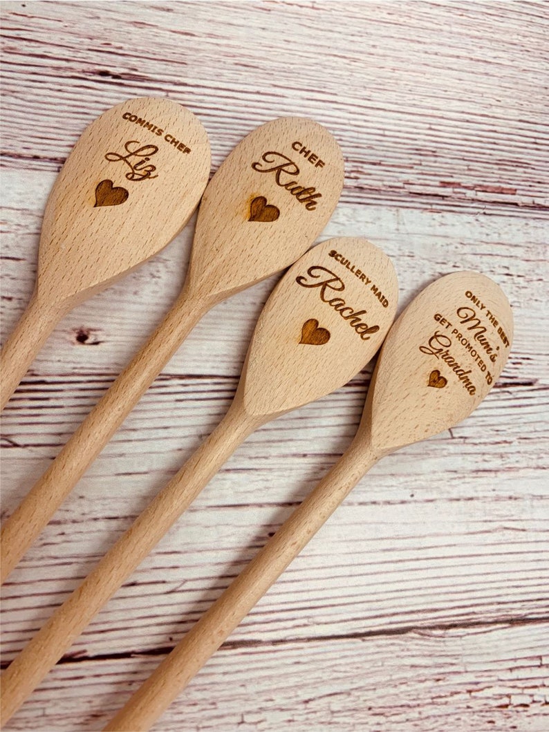 May include: Four wooden spoons with personalized engravings. The spoons are arranged in a row, with the top spoon reading "Commis Chef Liz", the second spoon reading "Chef Ruth", the third spoon reading "Scullery Maid Rachel", and the bottom spoon reading "Only the best Mum's get promoted to Grandma".