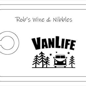 May include: A rectangular white serving board with a rounded cutout on the left side. The board features the black text Rob's Wine & Nibbles at the top and a black graphic below consisting of the word VANLIFE, pine trees, stars, and a camper van.