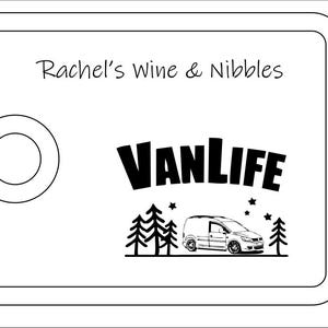 May include: A rectangular white serving board with a rounded cutout on the left side. The text Rachel's Wine & Nibbles is printed at the top. Below, the word VANLIFE appears above a graphic of a van, pine trees, and small stars.